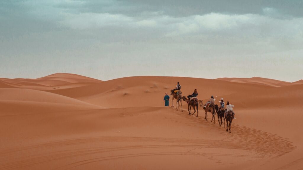Dunas de arena del Sahara en Merzouga al amanecer, campamento bereber con tiendas tradicionales, paseo en camello por el desierto de Marruecos.