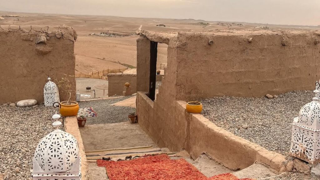 Campamento de lujo en el desierto de Agafay con jaimas iluminadas al atardecer y las montañas del Atlas de fondo. Reserva tus excursiones desde Marrakech con Haya Viajes.