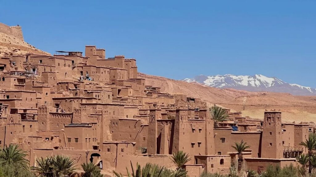 Vista aérea de la kasbah de Ait Ben Haddou con el río Ounila y el palmeral, rodeada de montañas. Reserva tu circuito por Marruecos con Haya Viajes.