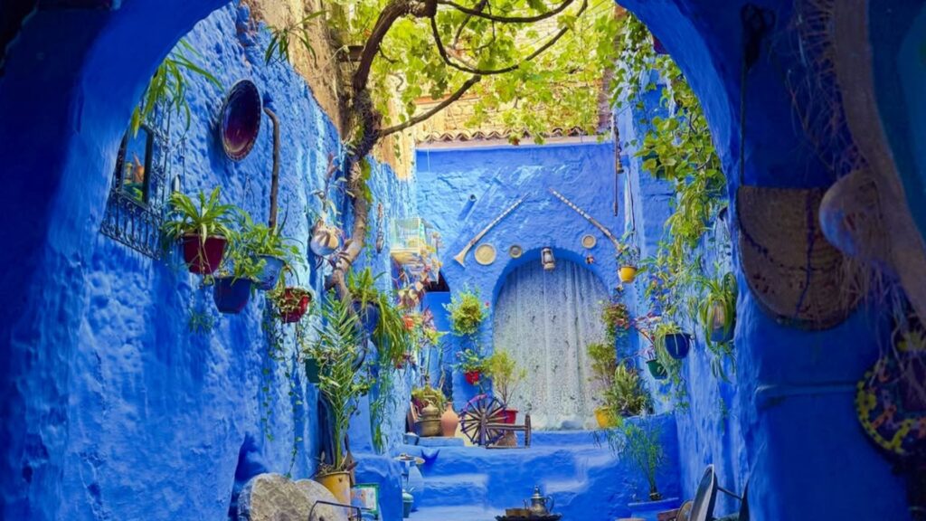 Tienda de artesanía en Chefchaouen con tejidos de lana de colores y fachada azul de fondo. Reserva tu circuito por Marruecos con Haya Viajes.