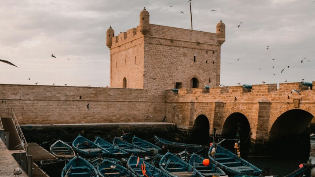 Vista de la muralla de la medina de Essaouira con el puerto pesquero y las gaviotas volando sobre el océano Atlántico. Reserva tu circuito por Marruecos con Haya Viajes.